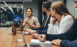 Young businesswoman leading a discussion during a meeting with her colleagues. Group of diverse businesspeople working together in a modern workplace. Business colleagues collaborating on a project.